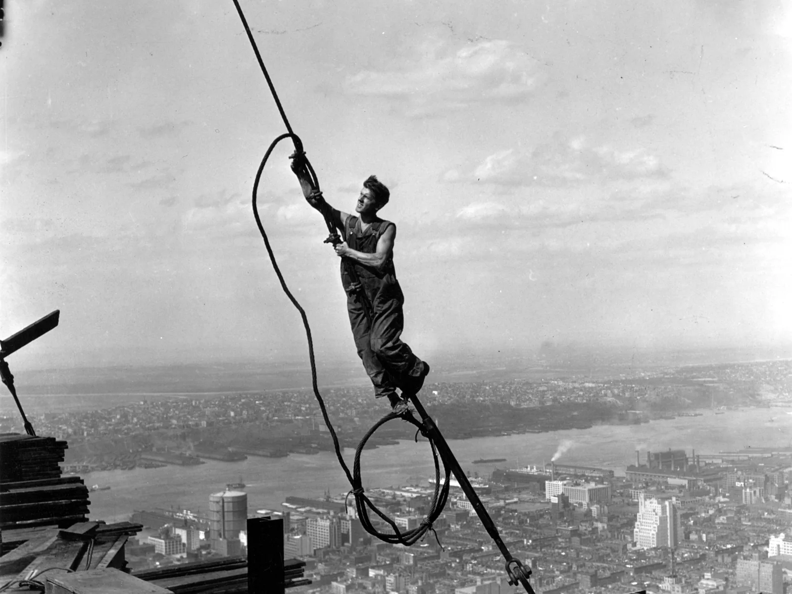 A steelworker swinging from a cable high above Manhattan and the Hudson River during the building of the Empire State Building.